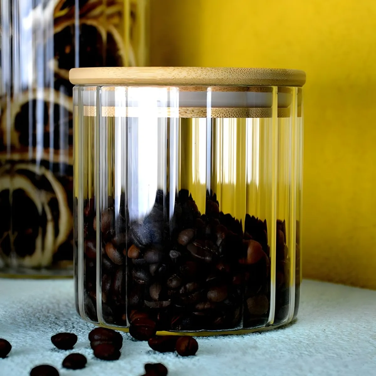 Clear fluted glass jar with bamboo lid, filled with coffee beans.