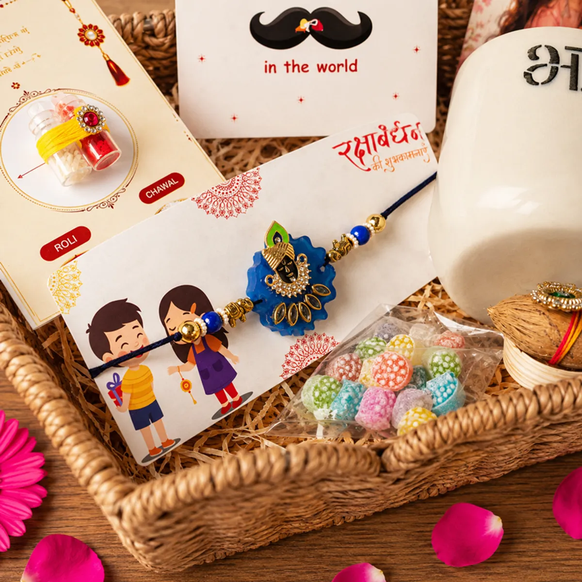 Close-up of Krishna rakhi, Bhai mug, festive cards and colourful sweets in a hamper