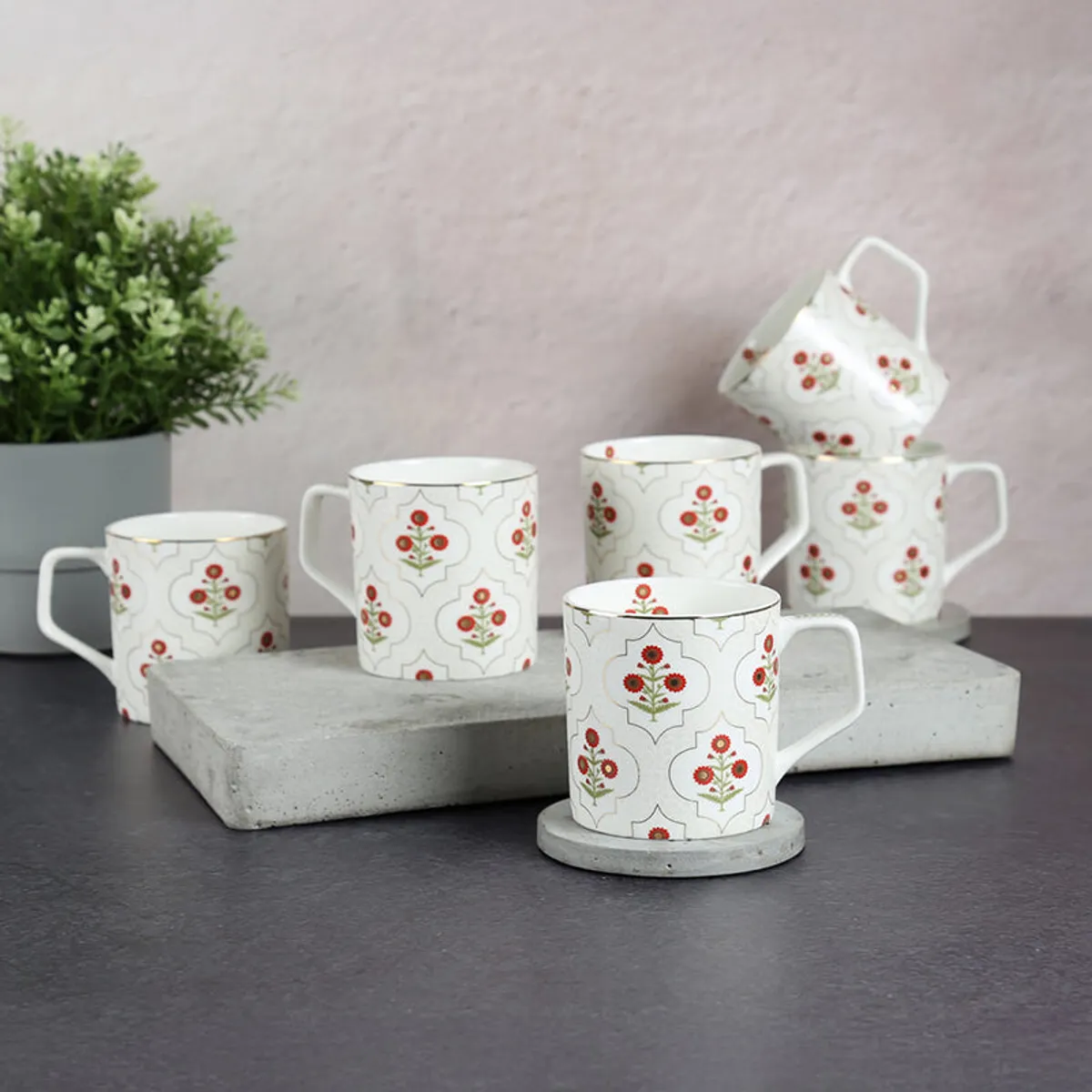 Six ivory tea cups with red floral motifs arranged on a tabletop.