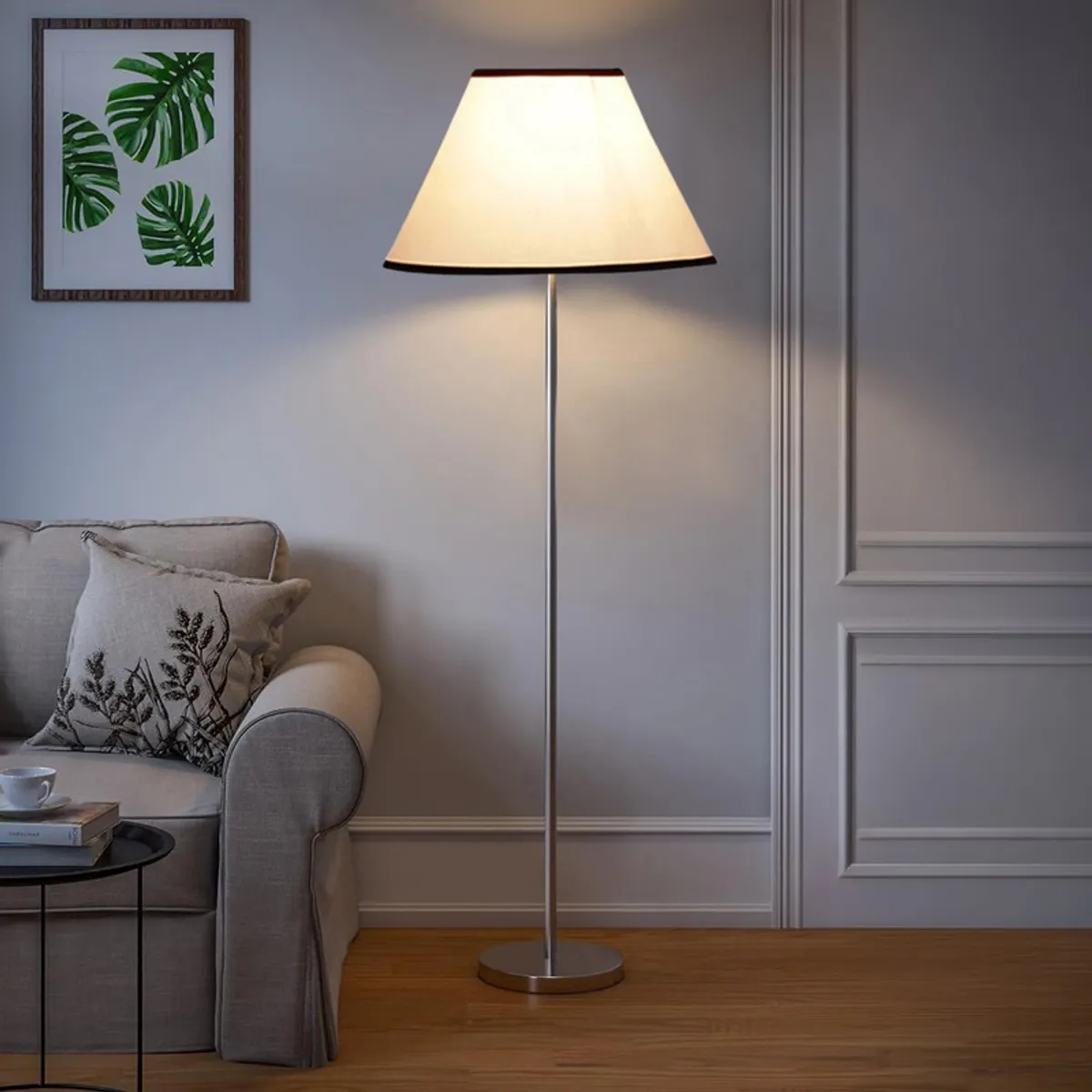Lit ivory floor lamp with tapered shade beside a neutral sofa