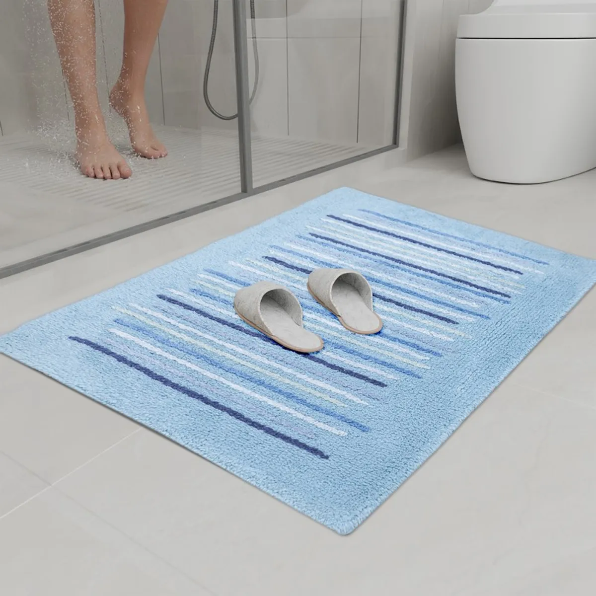 Blue striped bath mat placed outside a glass shower with slippers