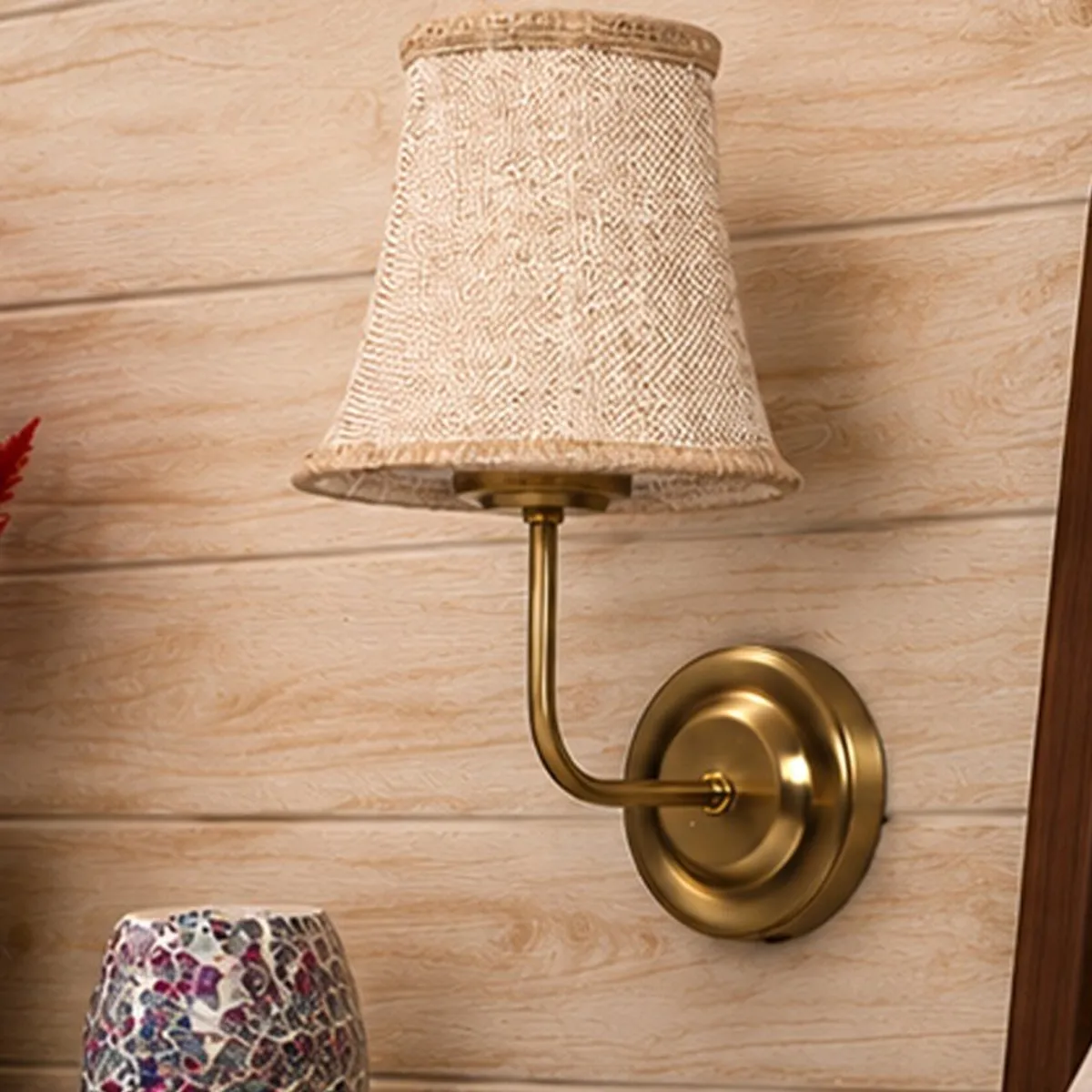 Front view of a beige jute shade on a gold-toned wall-mounted lamp