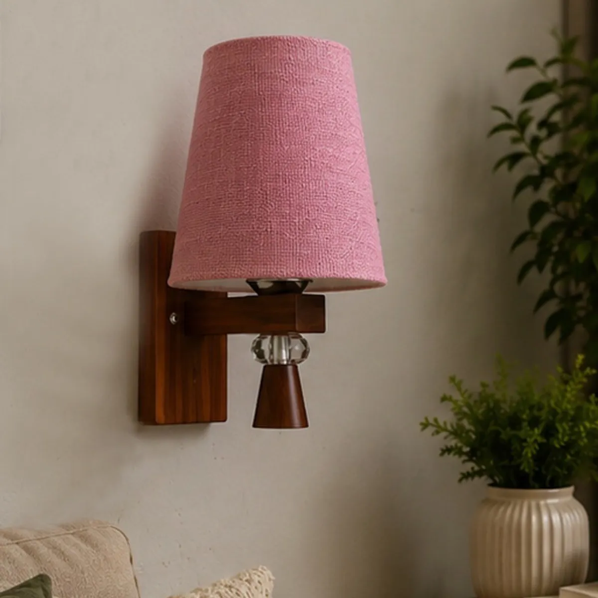 Close view of the pink textured shade and brown wooden wall lamp mount