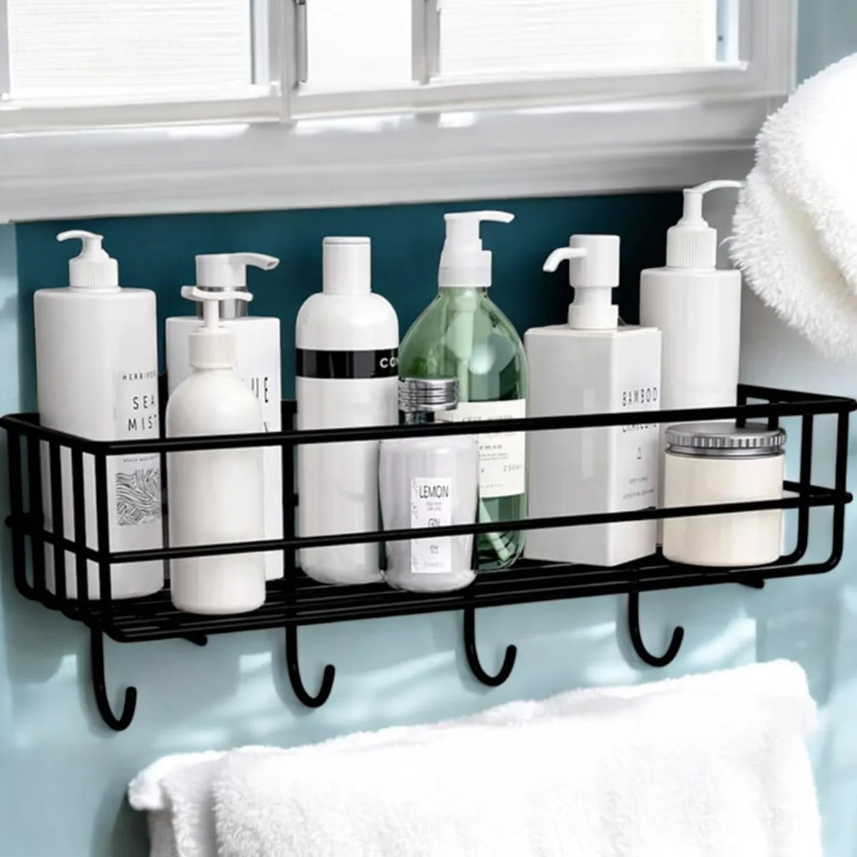 Black metal bathroom shelf with hooks holding bottles and a towel below