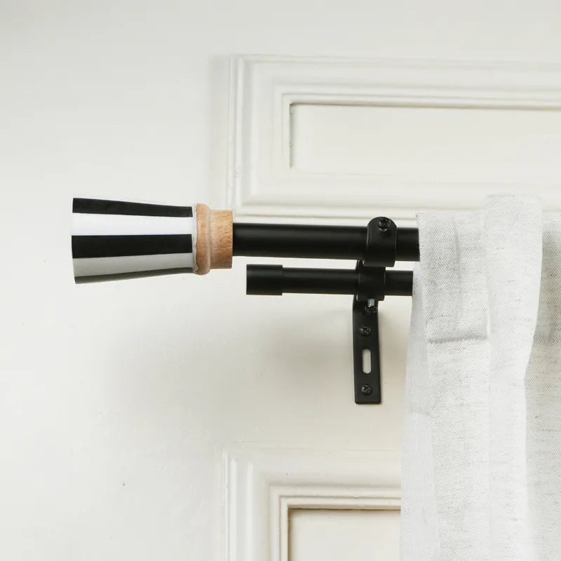 Black double curtain rod with black and white striped urn finial mounted on a wall