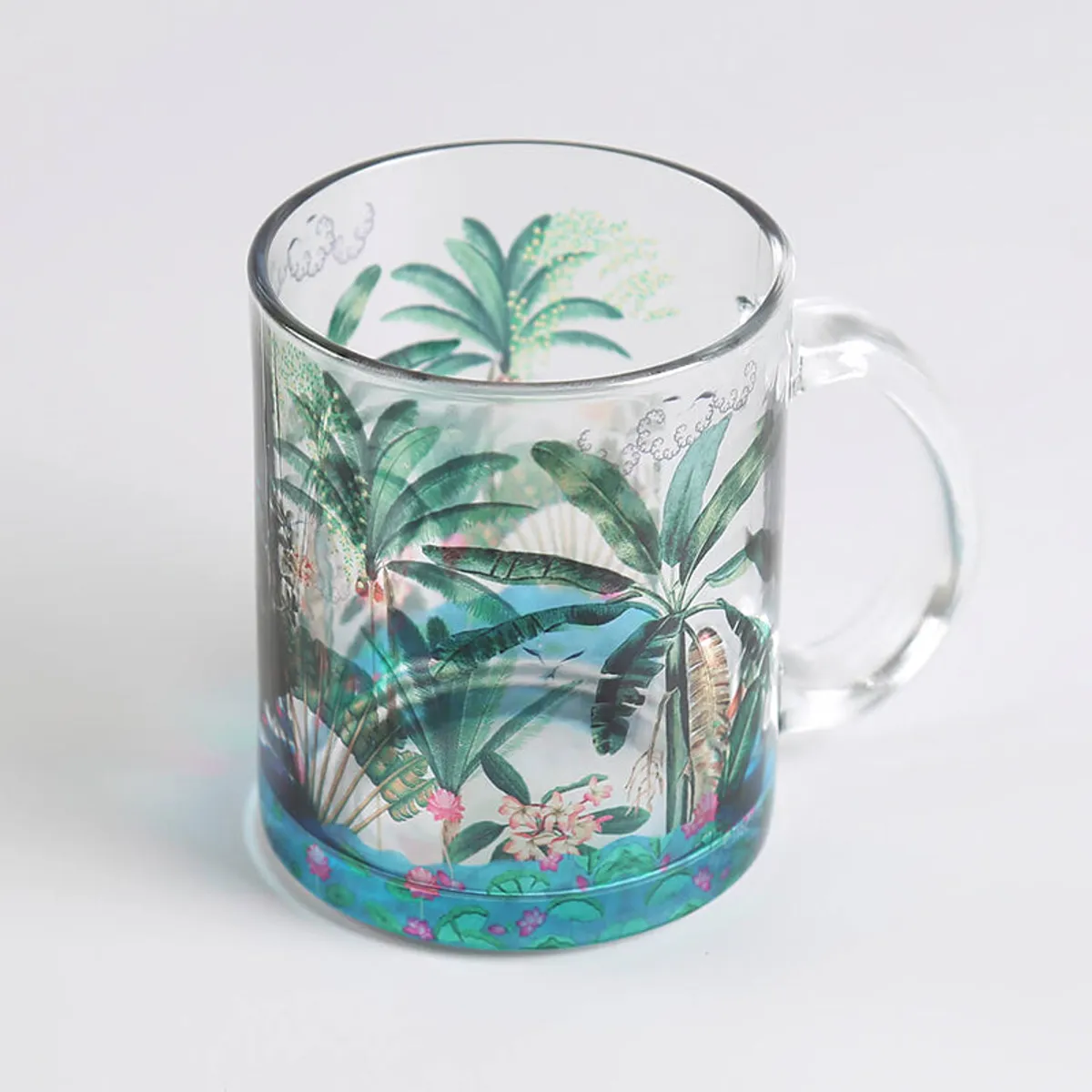 Close-up of a transparent glass mug with green palm and floral artwork