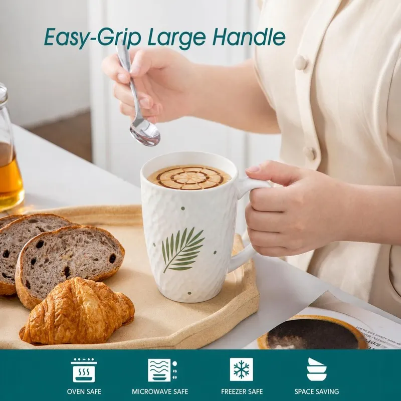 Person holding a white leaf-print mug beside breakfast foods