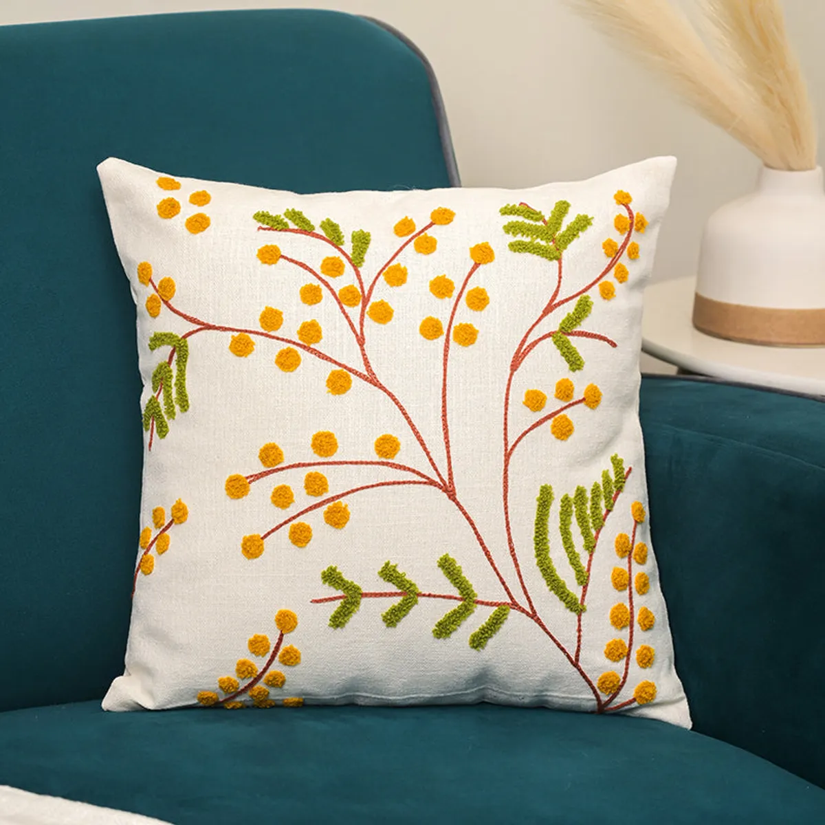 Ivory cushion cover with yellow and green floral embroidery on a teal chair