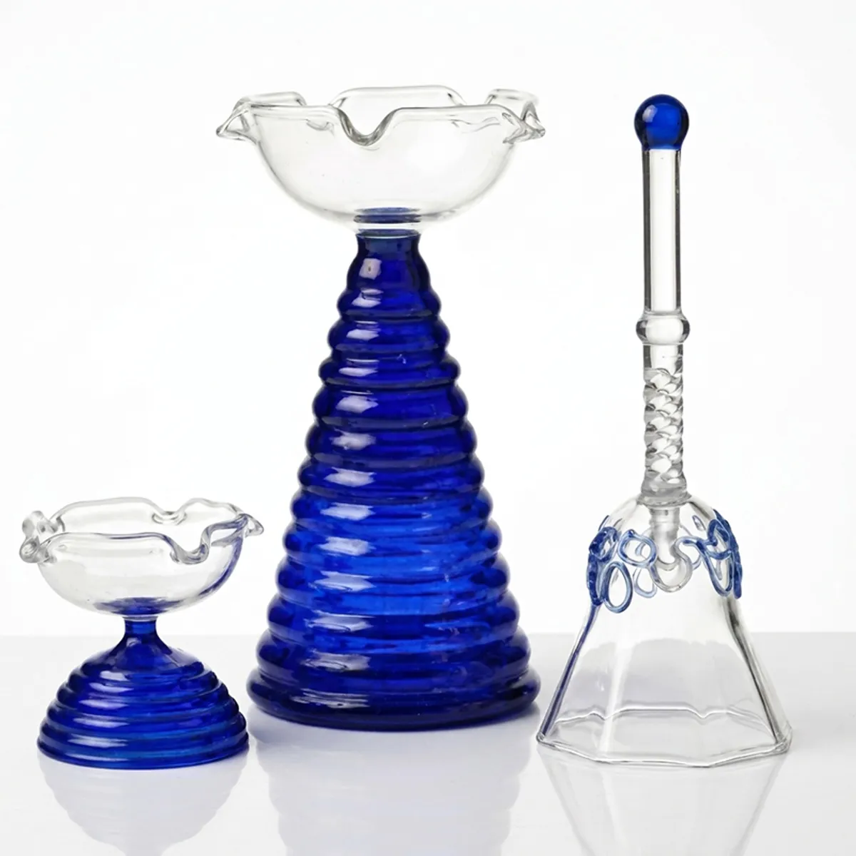 Blue and transparent glass diya and pooja bell set on a white background