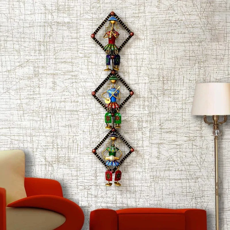 Vertical multicolour wall-mounted metal accent with three figurines on a textured wall