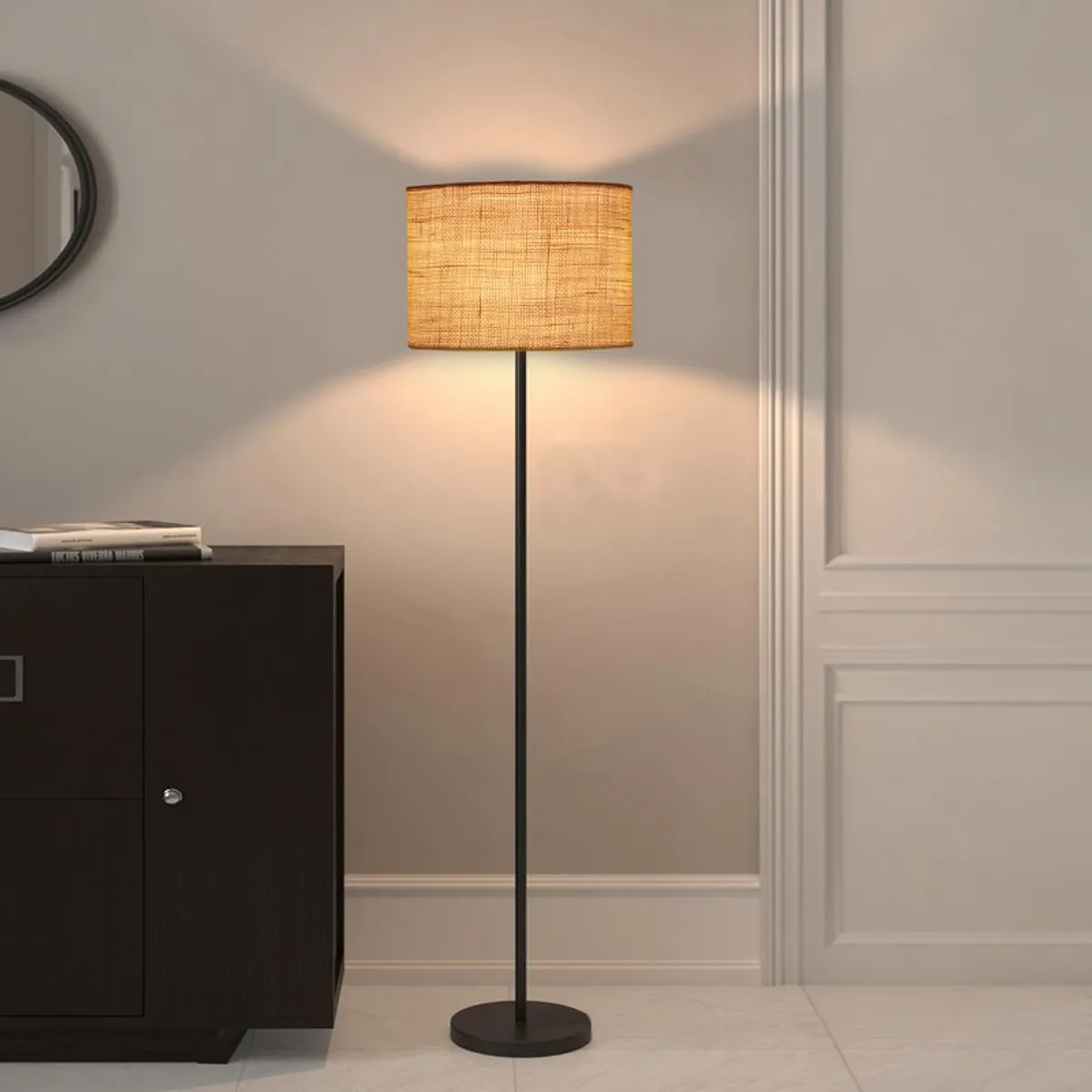 Lit floor lamp with cylindrical shade beside a dark cabinet and pale wall