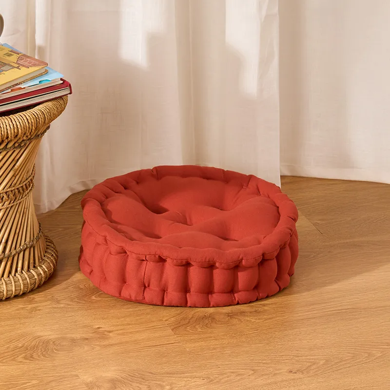 Round terracotta floor cushion with tufted top on a wooden floor