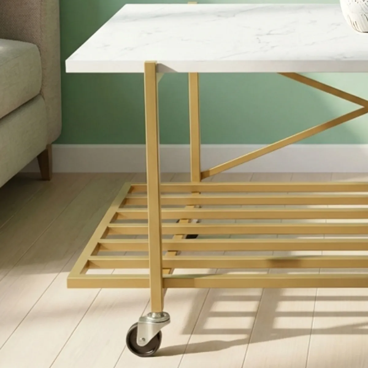 Close view of the coffee table's gold frame, lower shelf and wheeled leg