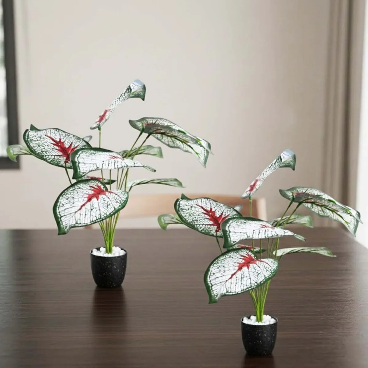 Two patterned-leaf artificial plants arranged on a dark wooden table