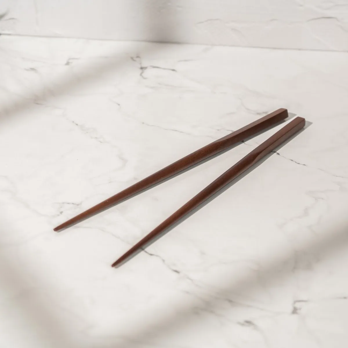 Two brown wooden chopsticks displayed on a light marble surface