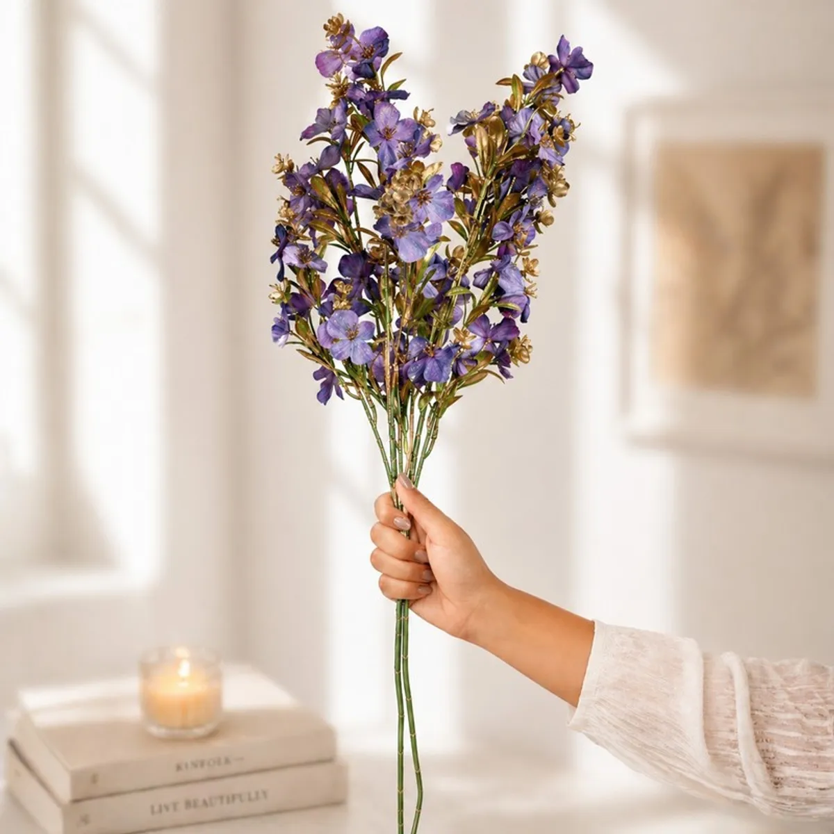 Hand holding a bunch of purple and gold artificial flower stems