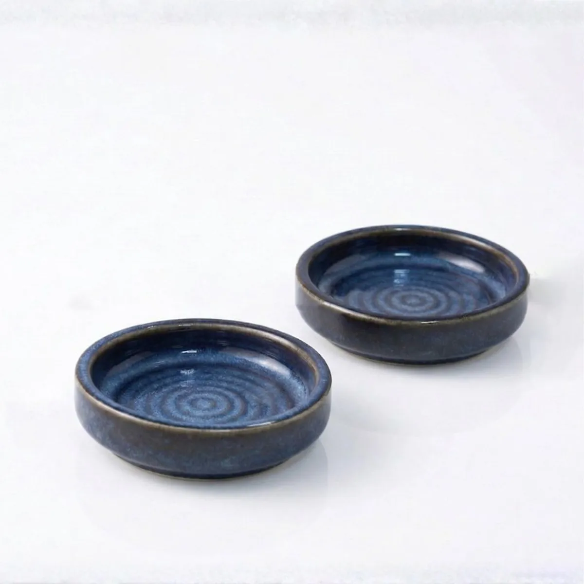 Two round blue ceramic dip bowls on a white surface