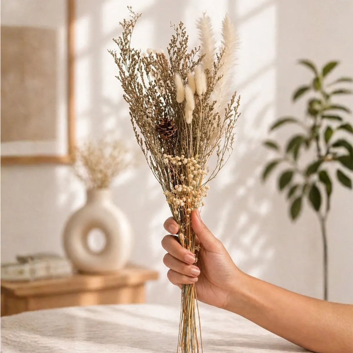 Hand holding a tall dried flower bouquet with soft beige and cream botanical stems