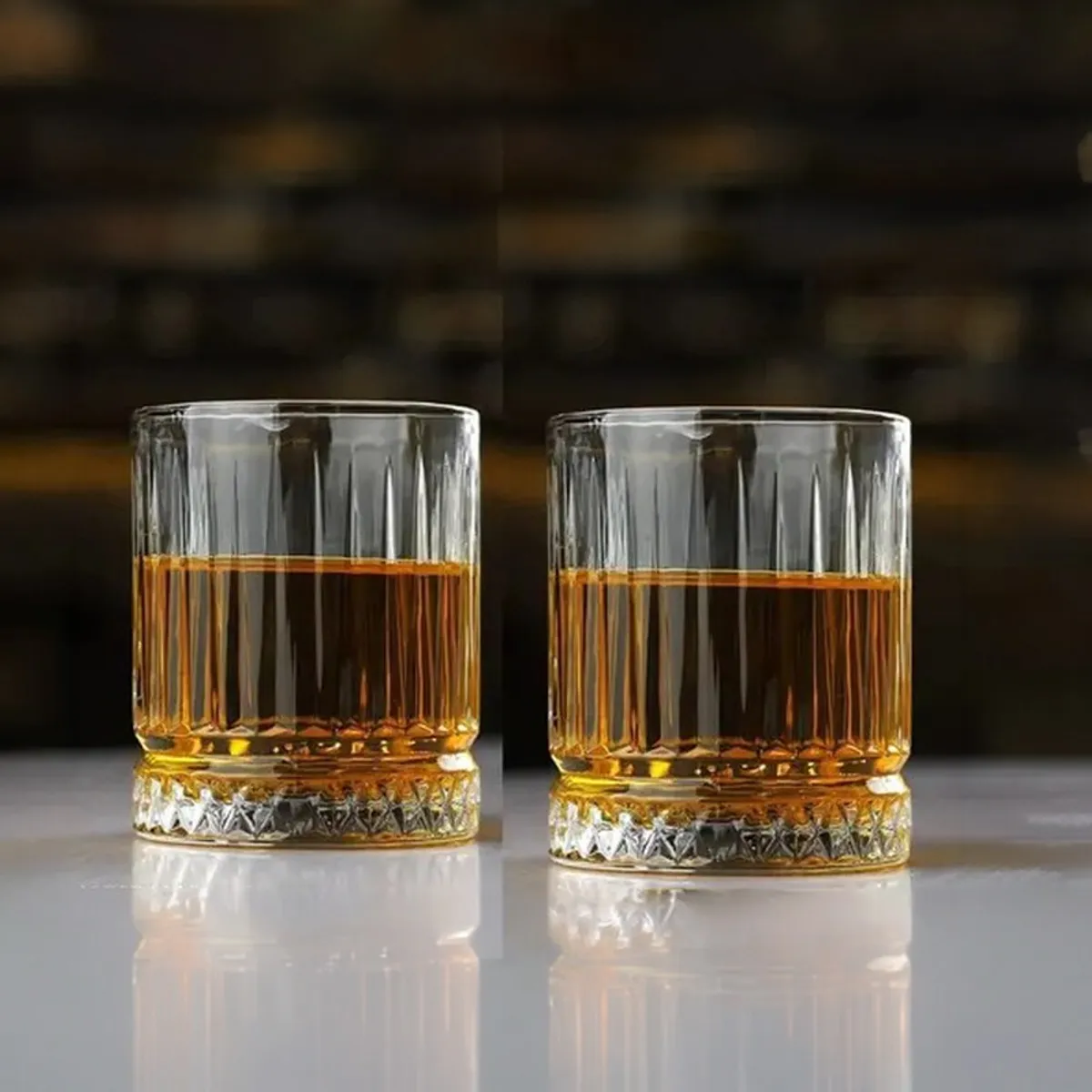 Two clear textured whiskey glasses filled with amber drink