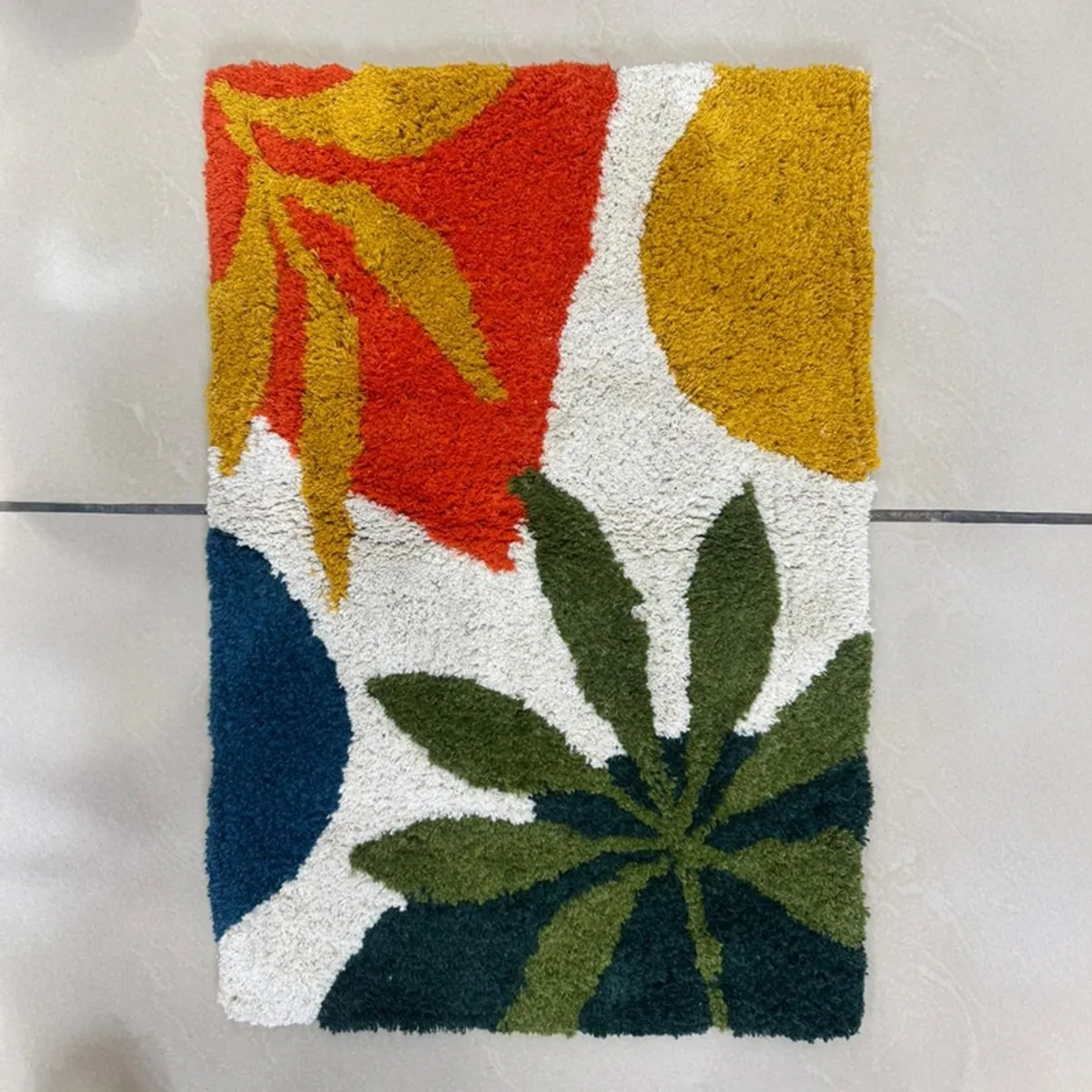 Vertical view of the colourful botanical bath mat on a tiled floor.