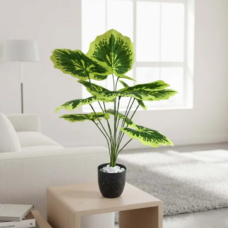 Single green and yellow patterned faux plant in a black pot beside a sofa.