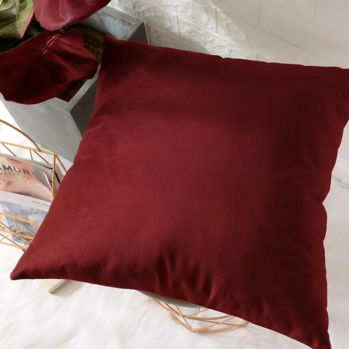Maroon velvet cushion cover placed on a bed beside decorative items