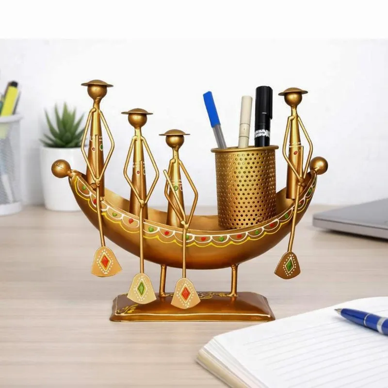 Decorative gold metal boat-shaped pen stand holding pens on a study desk