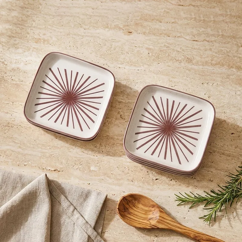 Two square white plates with maroon starburst design on a beige stone tabletop