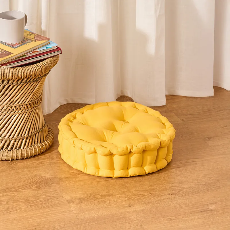 Round mustard yellow tufted floor cushion beside a woven side table