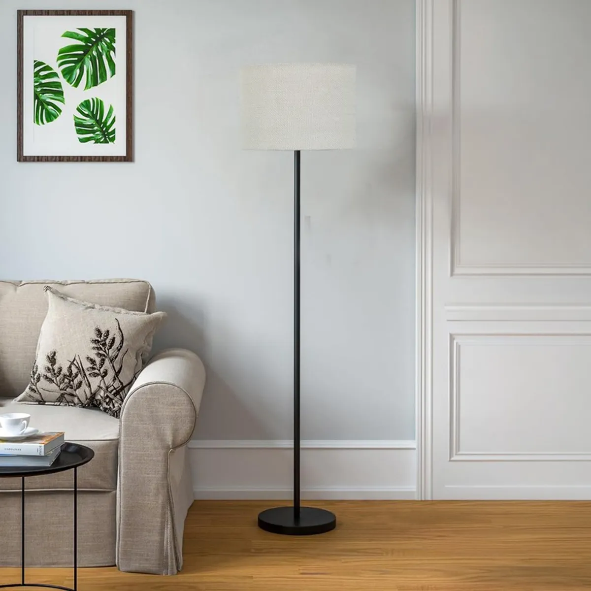 Floor lamp with white cylindrical shade and black stand beside a beige sofa