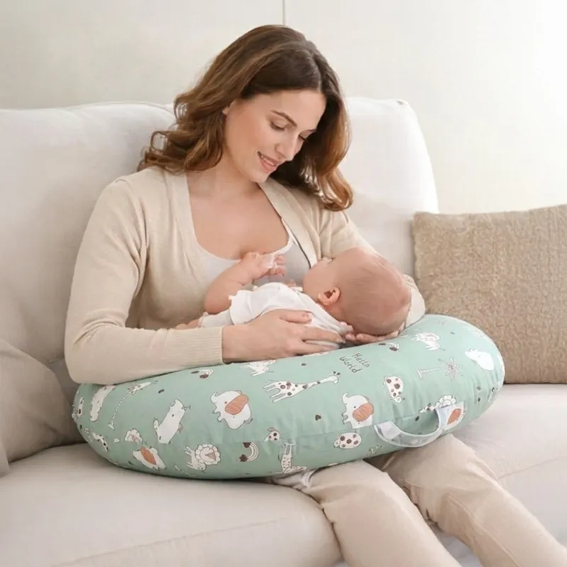 Woman using a green U-shape feeding pillow with playful animal print while feeding a baby