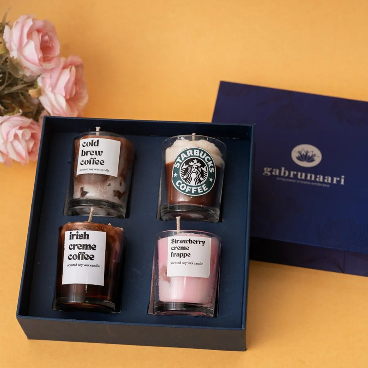 Four cylindrical glass jar candles arranged inside an open dark presentation box.