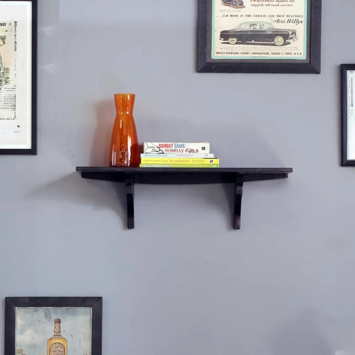 Black wooden wall shelf mounted on a grey wall with books and an orange vase