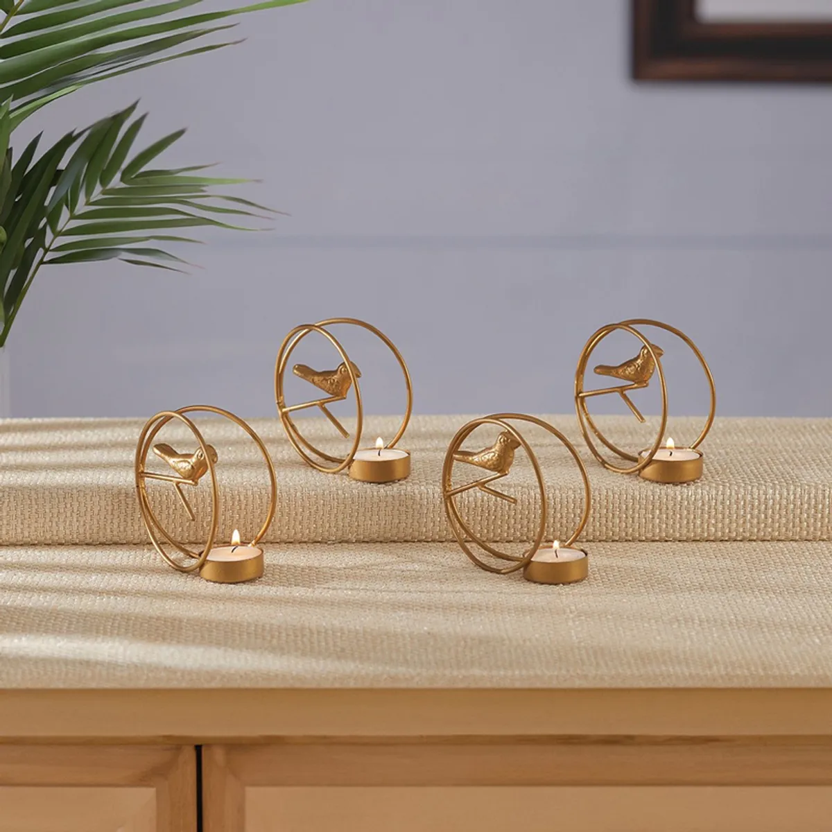 Four gold bird-themed tealight holders arranged on a layered surface