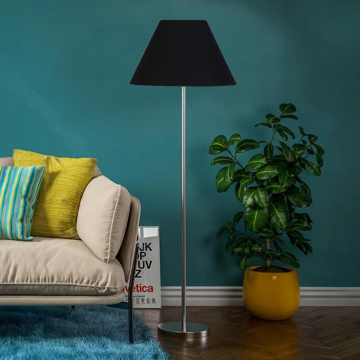 Black floor lamp with slim metal stand styled beside a sofa and potted plant
