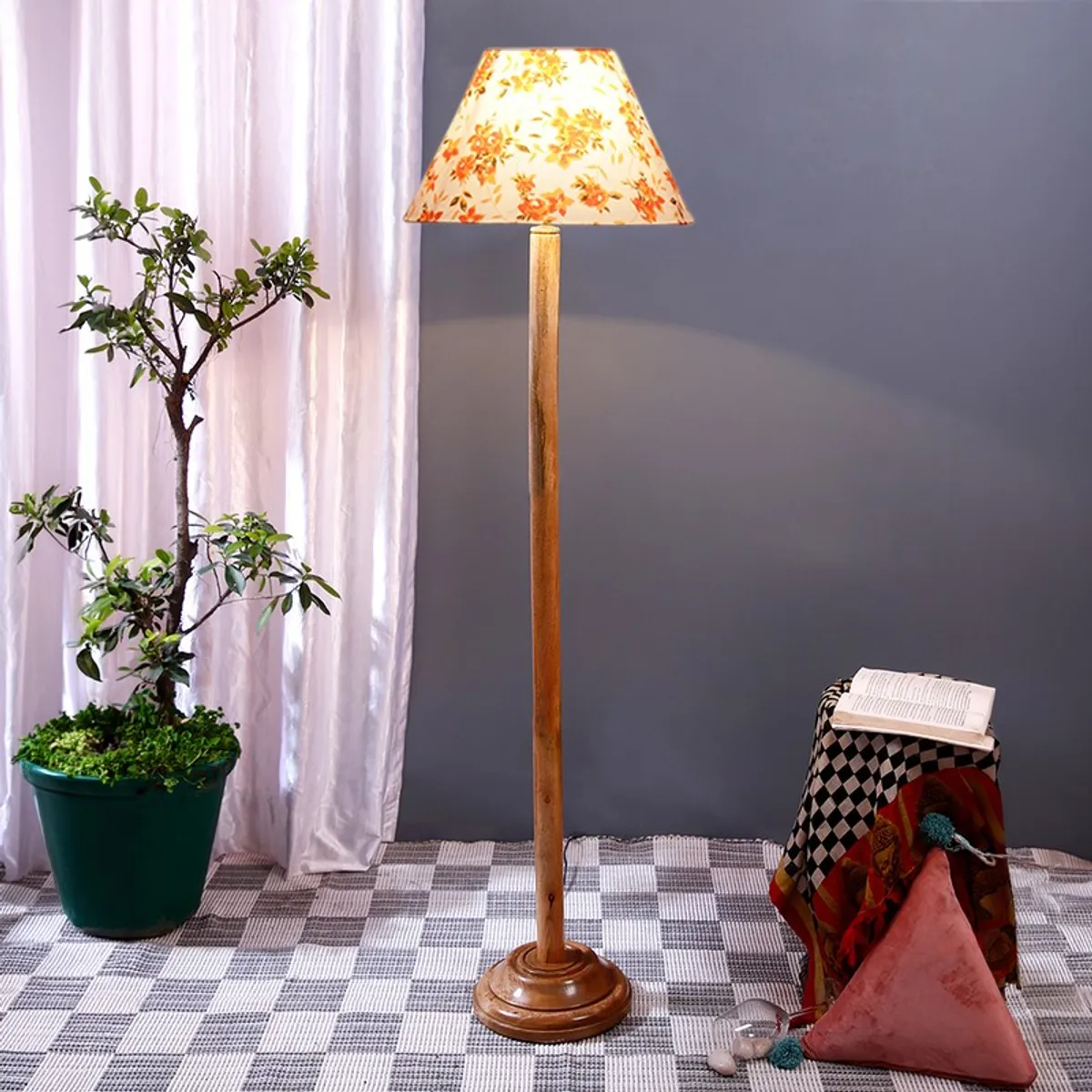 Wooden floor lamp with floral shade placed beside a potted plant and side stool