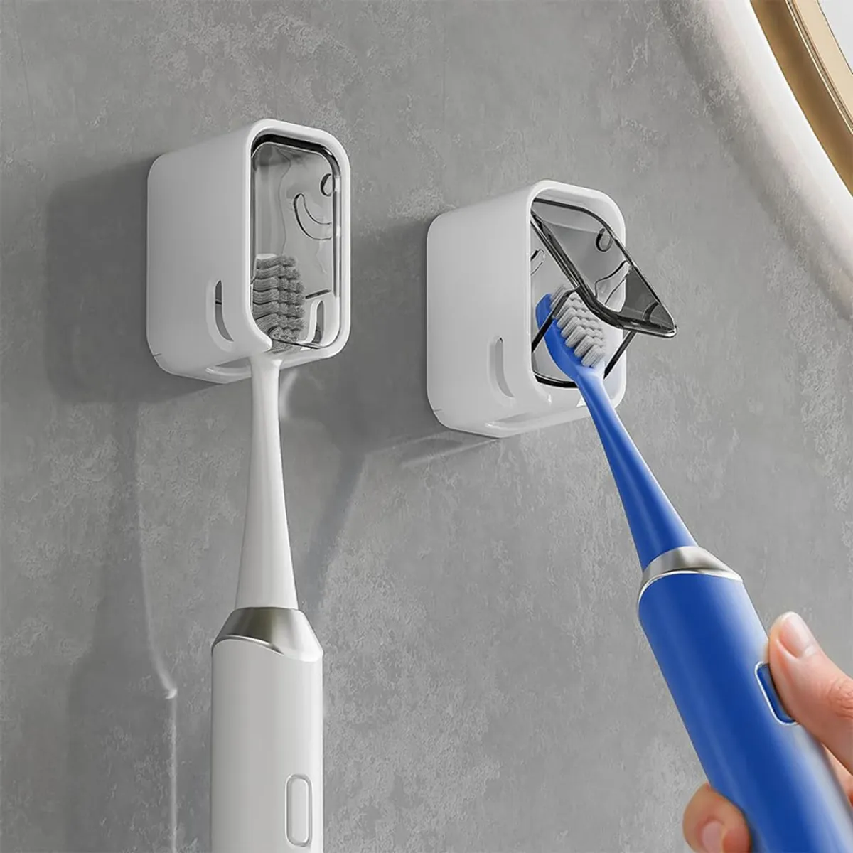 Close-up of two white toothbrush holders with clear flip covers mounted on a grey wall
