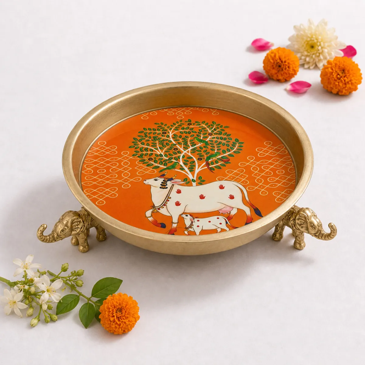 Round orange and gold urli showing Kamdhenu and Tree of Life artwork
