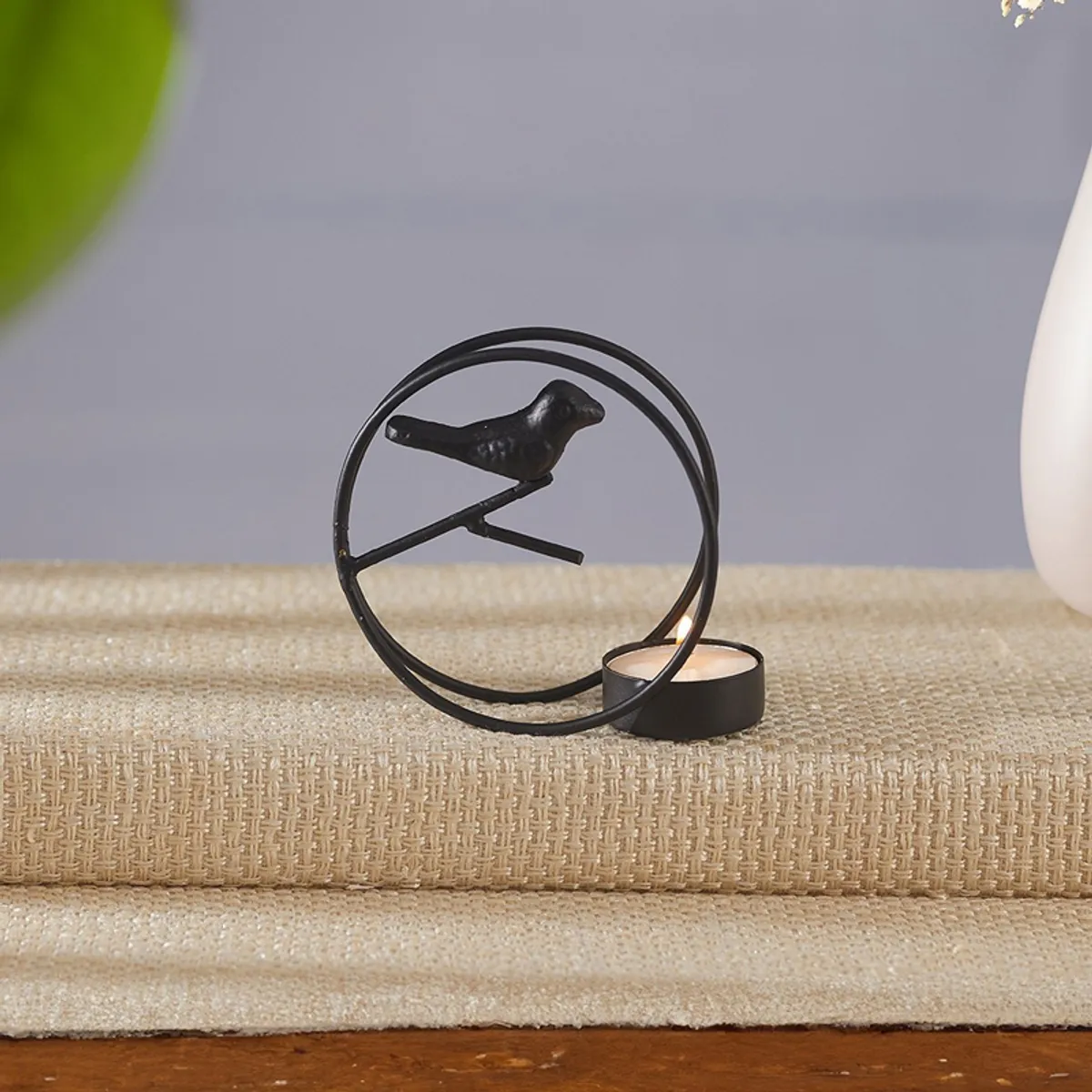 Close-up of a black circular bird tealight holder with a lit candle