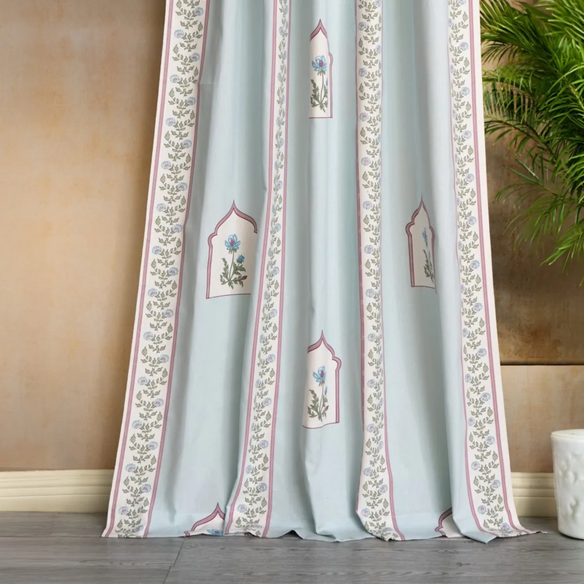 Close view of light blue curtains with floral borders and arch motifs
