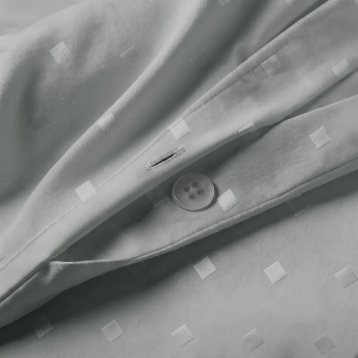 Close-up of grey duvet cover fabric with raised square dot detailing and button closure