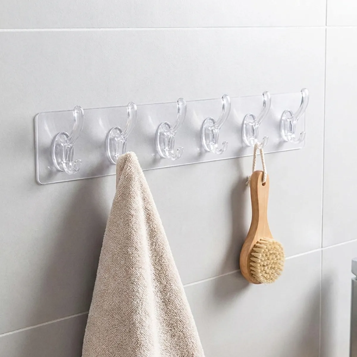 Transparent six-hook strip mounted in a bathroom with a towel and brush