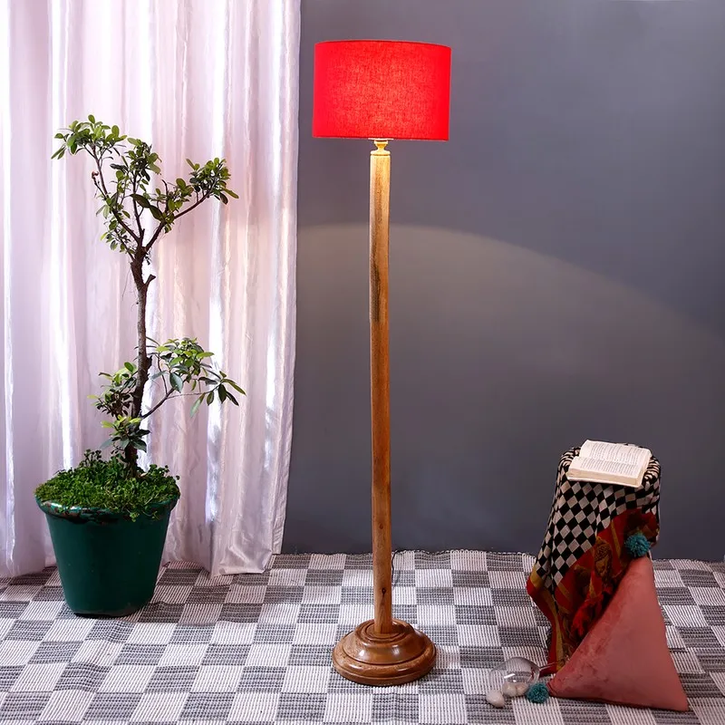 Wooden floor lamp with red drum shade lit in a styled indoor corner