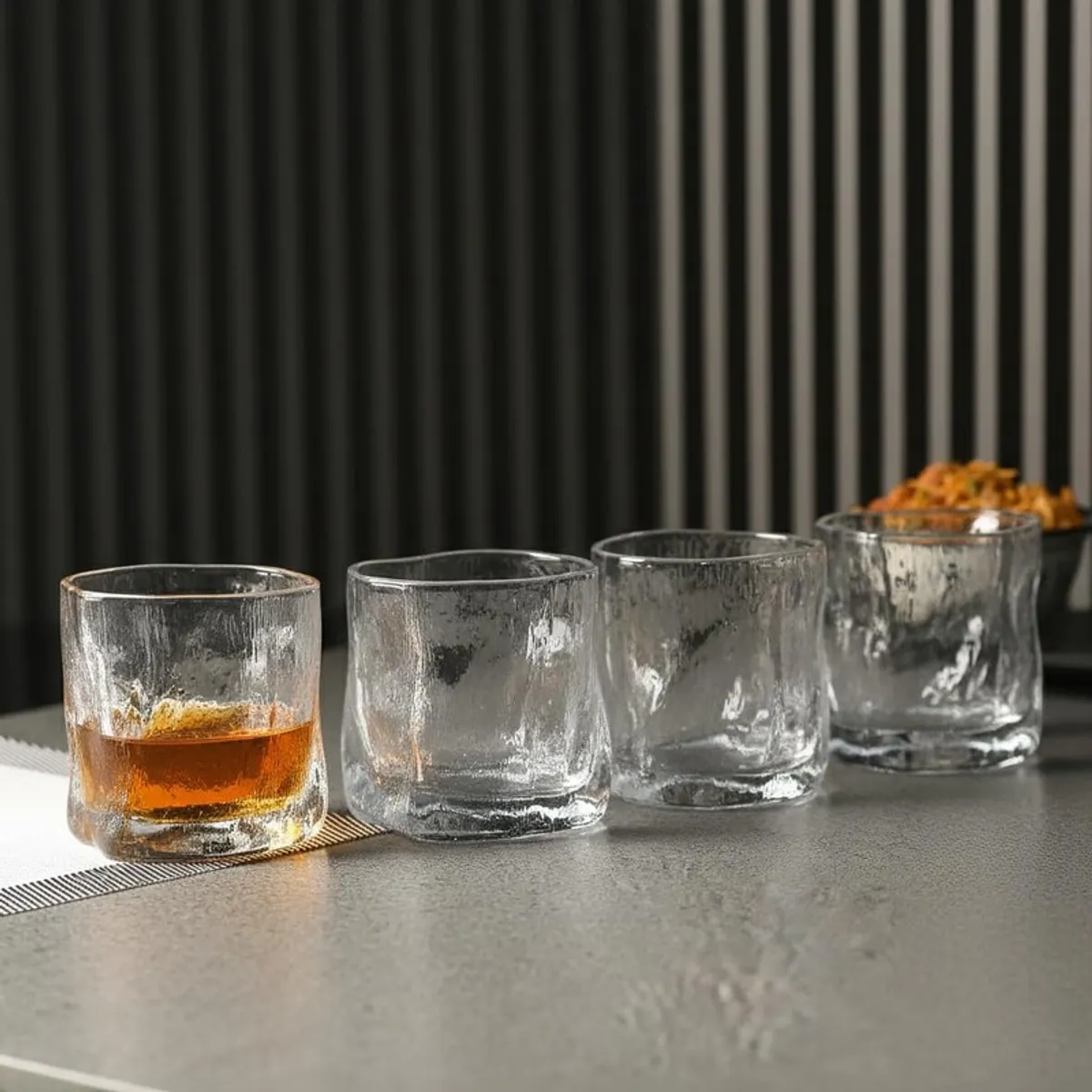 Four clear whiskey glasses lined up on a tabletop