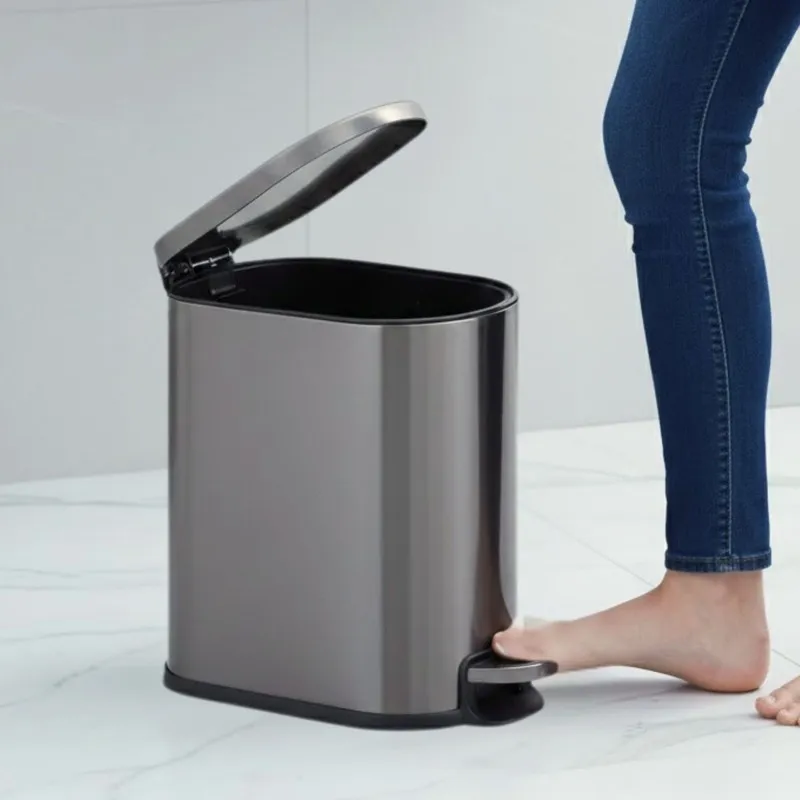 Black metal pedal dustbin with lid open beside a foot pressing the pedal