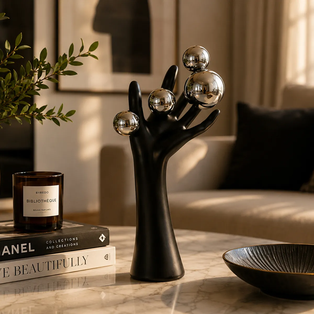 Matte black hand sculpture with reflective silver spheres styled on a coffee table