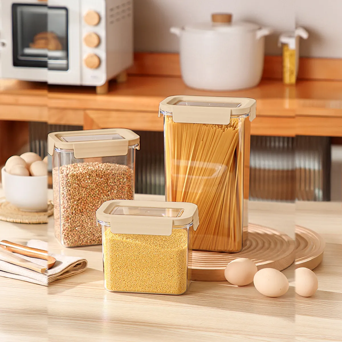 Three clear pantry containers with beige lids holding grains and pasta in a kitchen