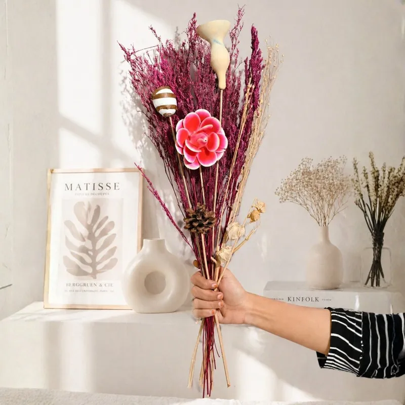 Hand holding a pink dried flower bouquet with decorative stems