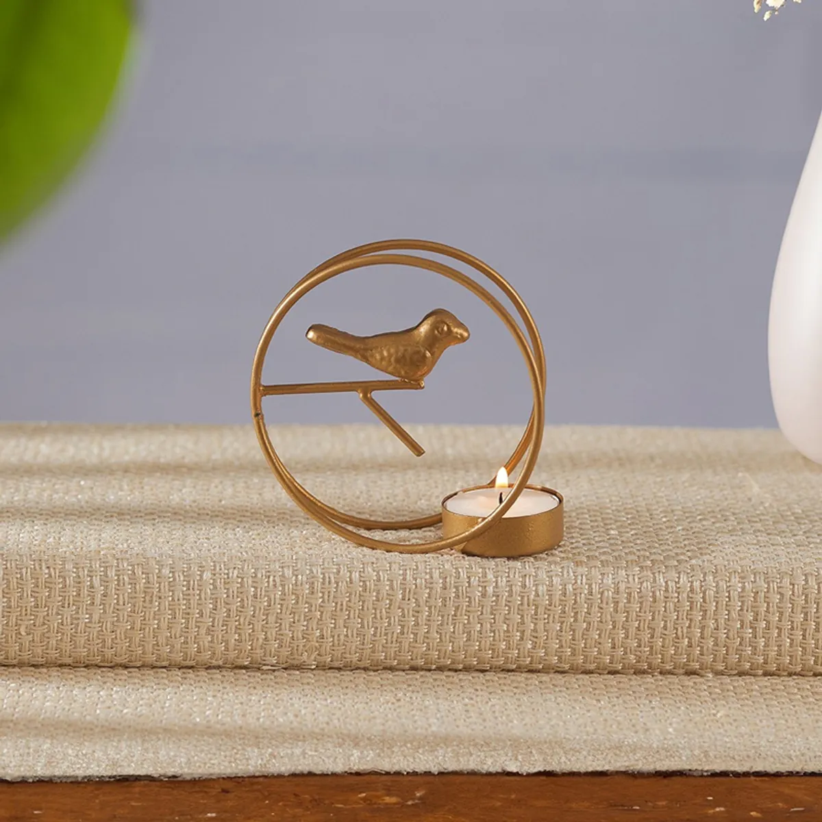 Single gold bird-themed tealight holder with a lit candle