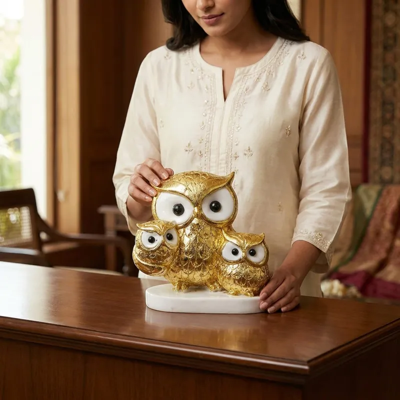 Person holding a gold and white owl family showpiece on a wooden table